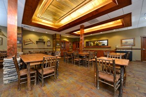 A restaurant with wooden tables and chairs, a bar area, and a high ceiling with exposed beams.
