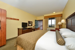 A hotel room with a bed, a desk with a television, a chair, a window with curtains, and a door. - The Cody Hotel (Cody)