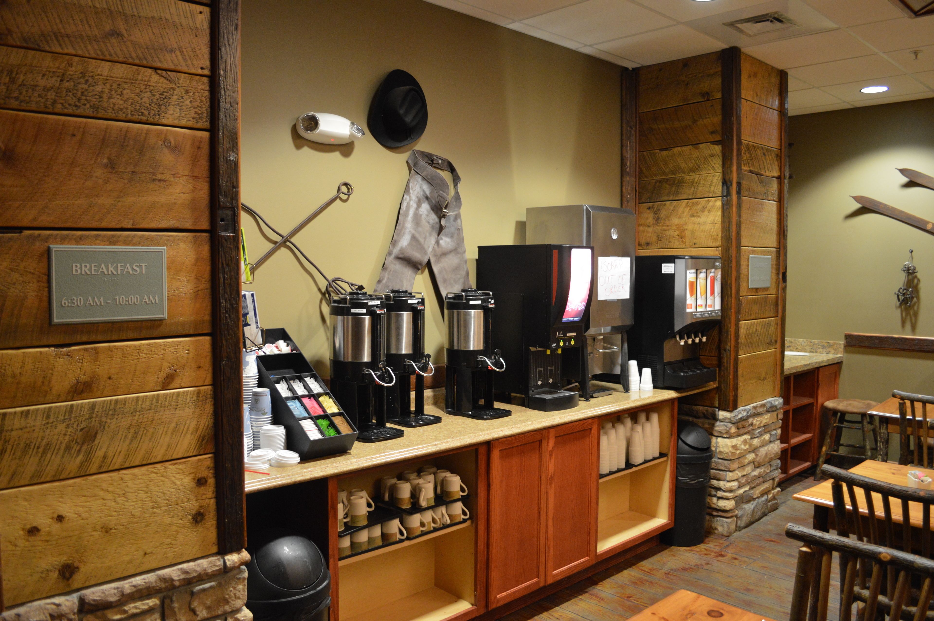 A breakfast area with coffee machines, a menu board, and a sign indicating breakfast hours.