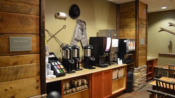 A breakfast area with coffee machines, a menu board, and a sign indicating breakfast hours.