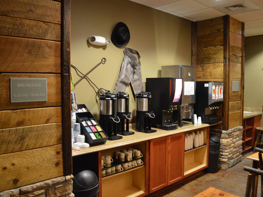 A breakfast area with coffee machines, a menu board, and a sign indicating breakfast hours.