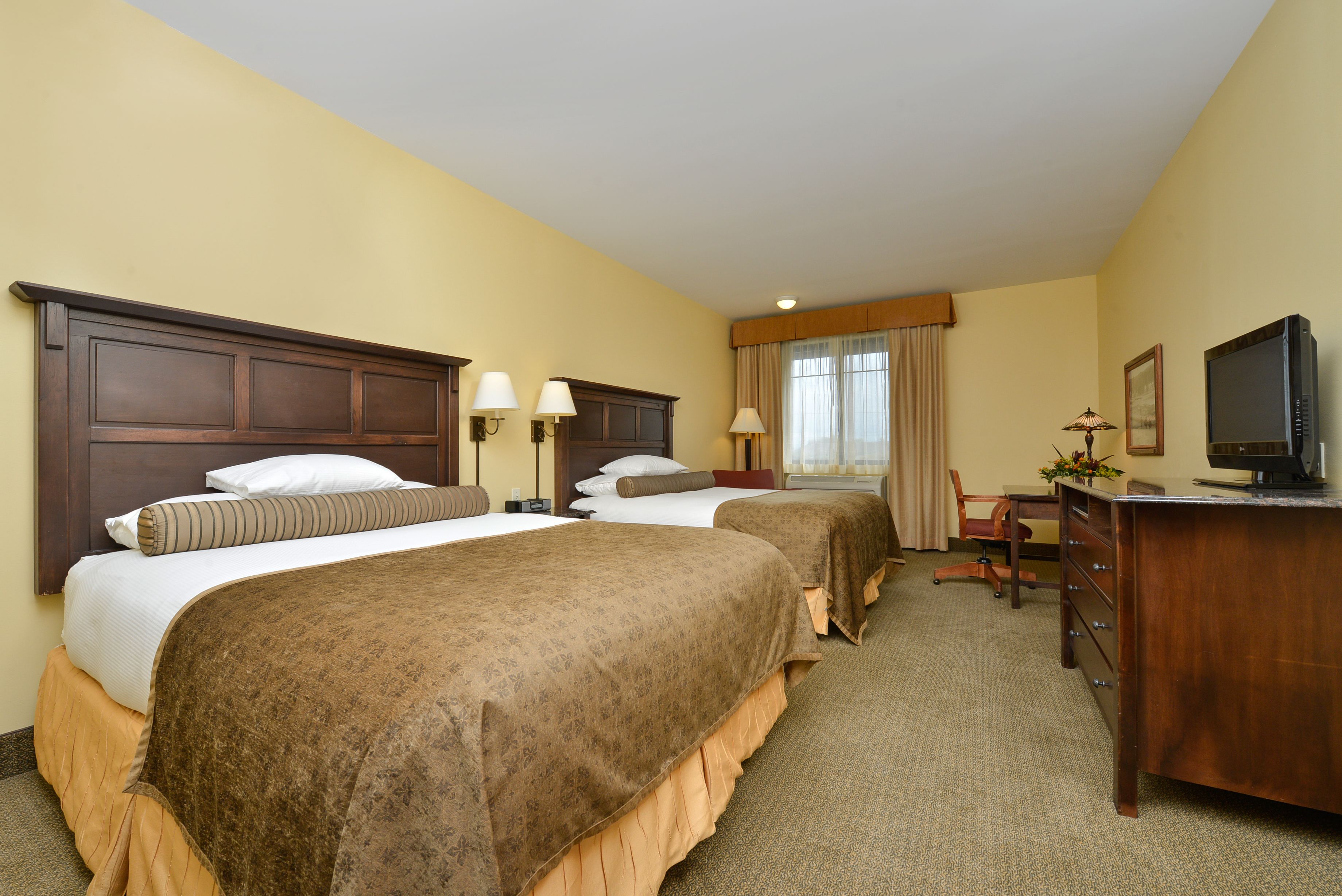 A hotel room with two beds, a desk, a chair, a television, and a window with curtains.