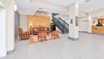 Eine geräumige Lobby mit moderner Treppe, einer Rezeption und einer Sitzecke mit Sofa und Sesseln.