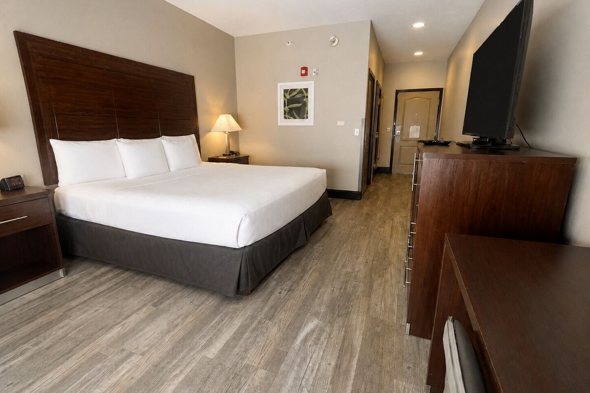 A hotel room with a large bed, a desk, a television, and a door leading to a bathroom.
