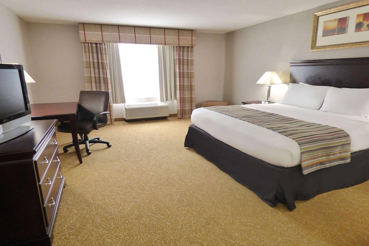 Hotelkamer met een bed, bureau, stoel, televisie en raam met gordijnen.