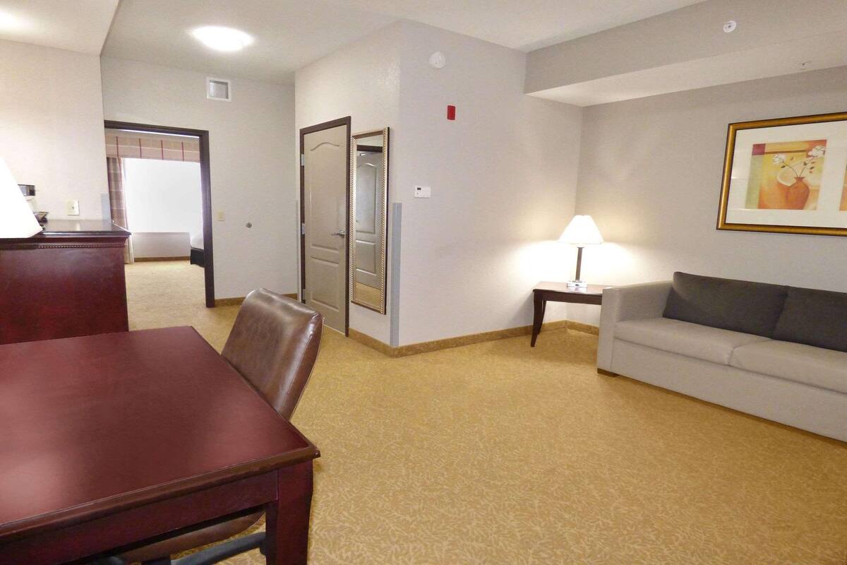 Een hotelkamer met een eettafel, een bank, een lamp en een ingelijste foto aan de muur.