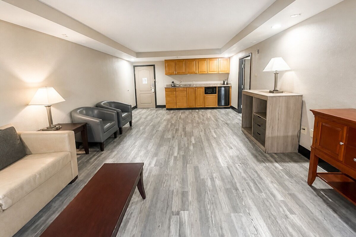 A modern living room with a sofa, two armchairs, a coffee table, and a kitchen area with wooden cabinets and appliances.