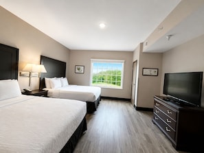 A hotel room with two beds, a television, a dresser, and a window with a view of greenery.