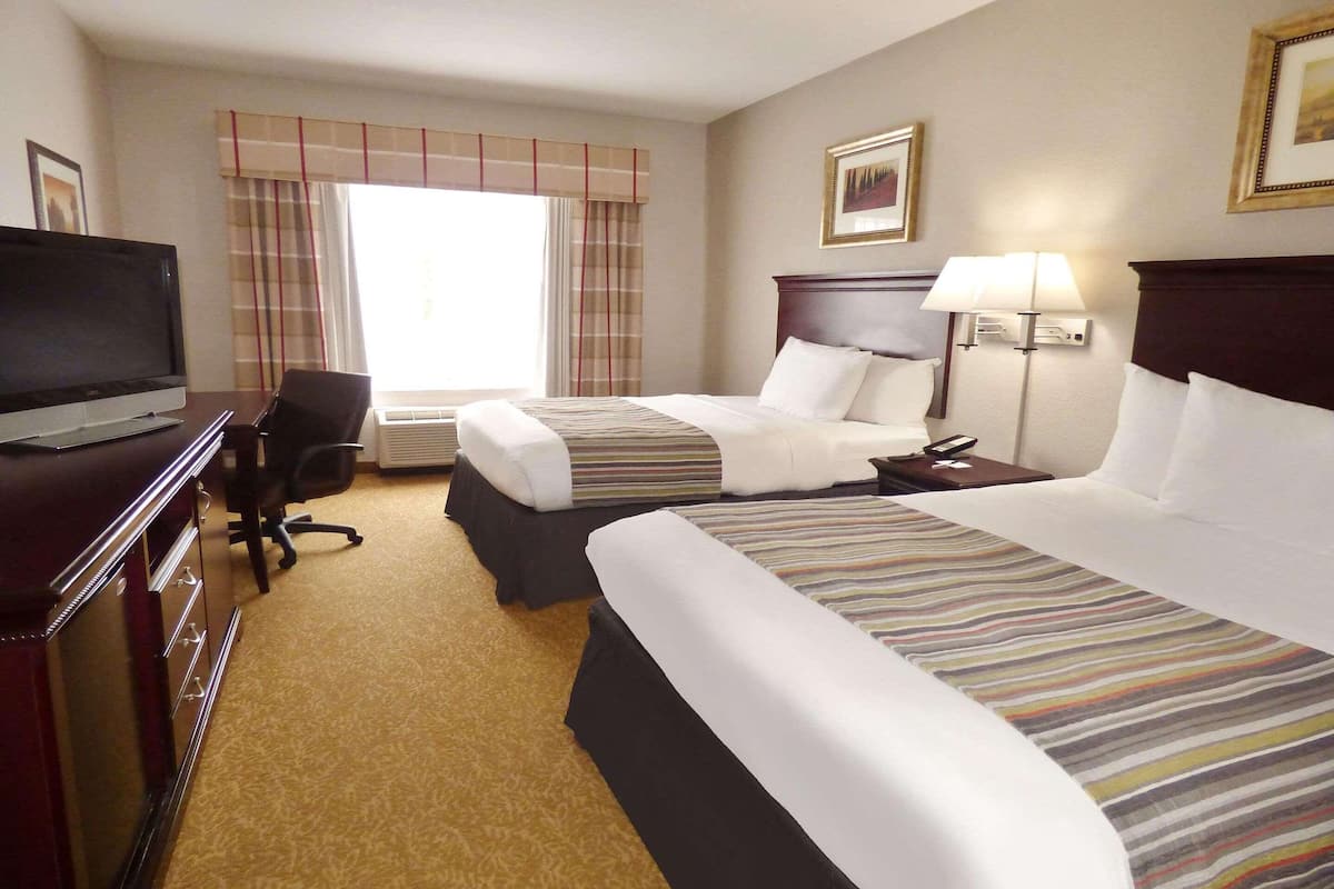 Een hotelkamer met twee bedden, een bureau met een televisie, een stoel en een lamp.