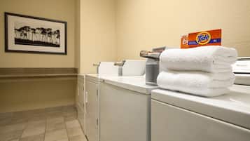 A laundry area with a Tide detergent box, a folded white towel, and a framed picture on the wall.