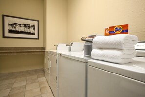 A laundry area with a Tide detergent box, a folded white towel, and a framed picture on the wall. - Country Inn & Suites by Radisson, Pensacola West, FL (Pensacola)