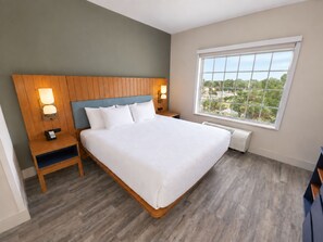 A hotel room with a large bed, wooden headboard, bedside lamps, a nightstand, a window with a view, and a built-in heater.