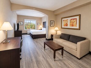Habitación de hotel con cama, sofá, mesa de centro, escritorio y televisor.