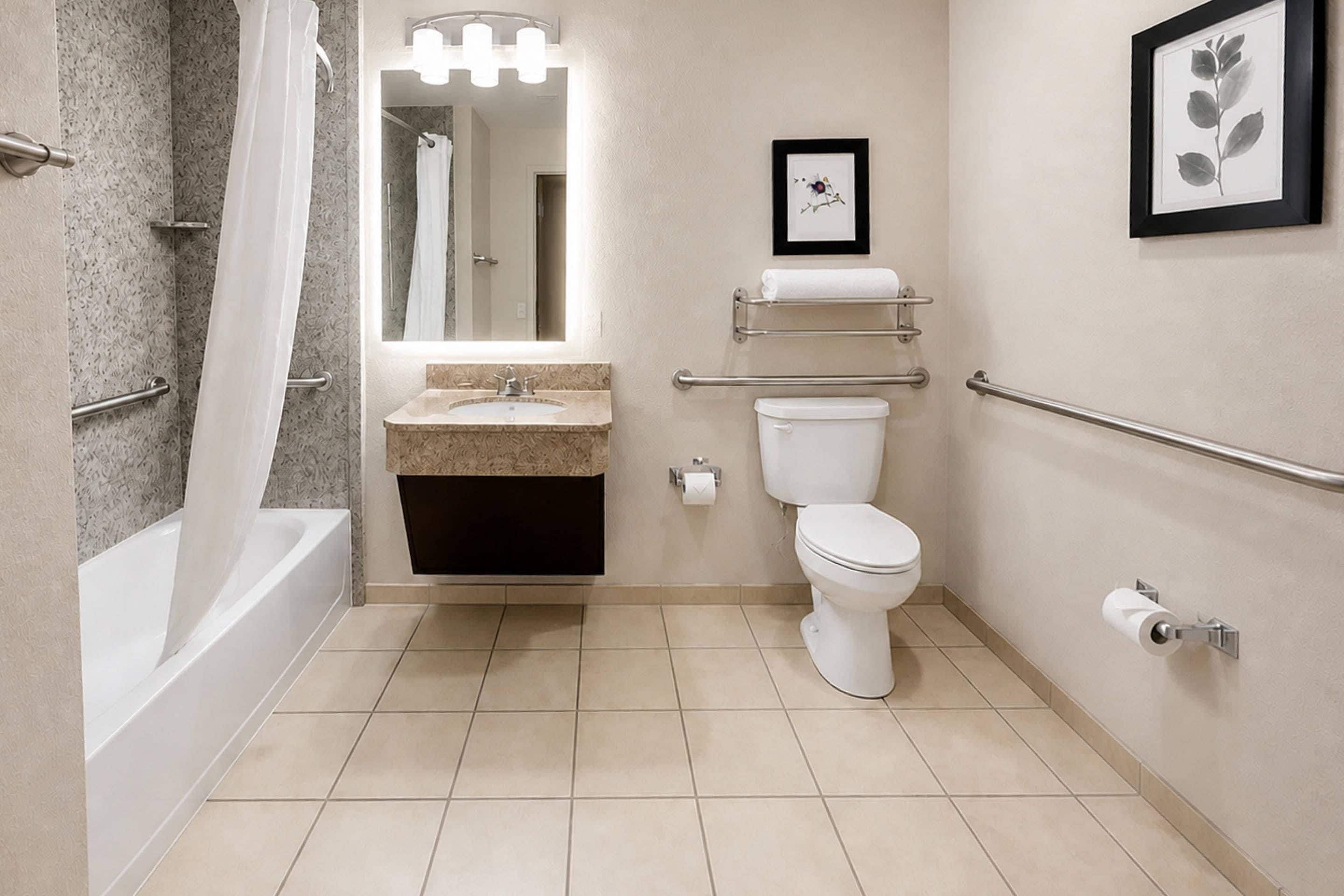 A modern bathroom with a bathtub, toilet, sink, and handrails.