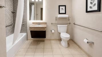 A modern bathroom with a bathtub, toilet, sink, and handrails.