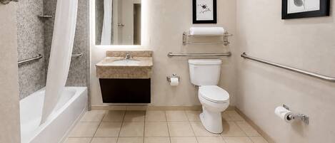 A modern bathroom with a bathtub, toilet, sink, and handrails.