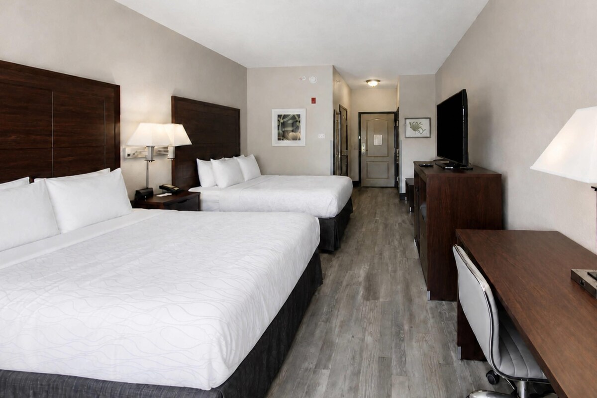 Een hotelkamer met twee bedden, een bureau, een televisie en een deur naar een gang.