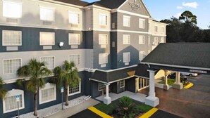 A multi-story hotel with a Country Inn & Suites sign, featuring a central entrance with a covered patio and palm trees. - Country Inn & Suites by Radisson, Pensacola West, FL (Pensacola)
