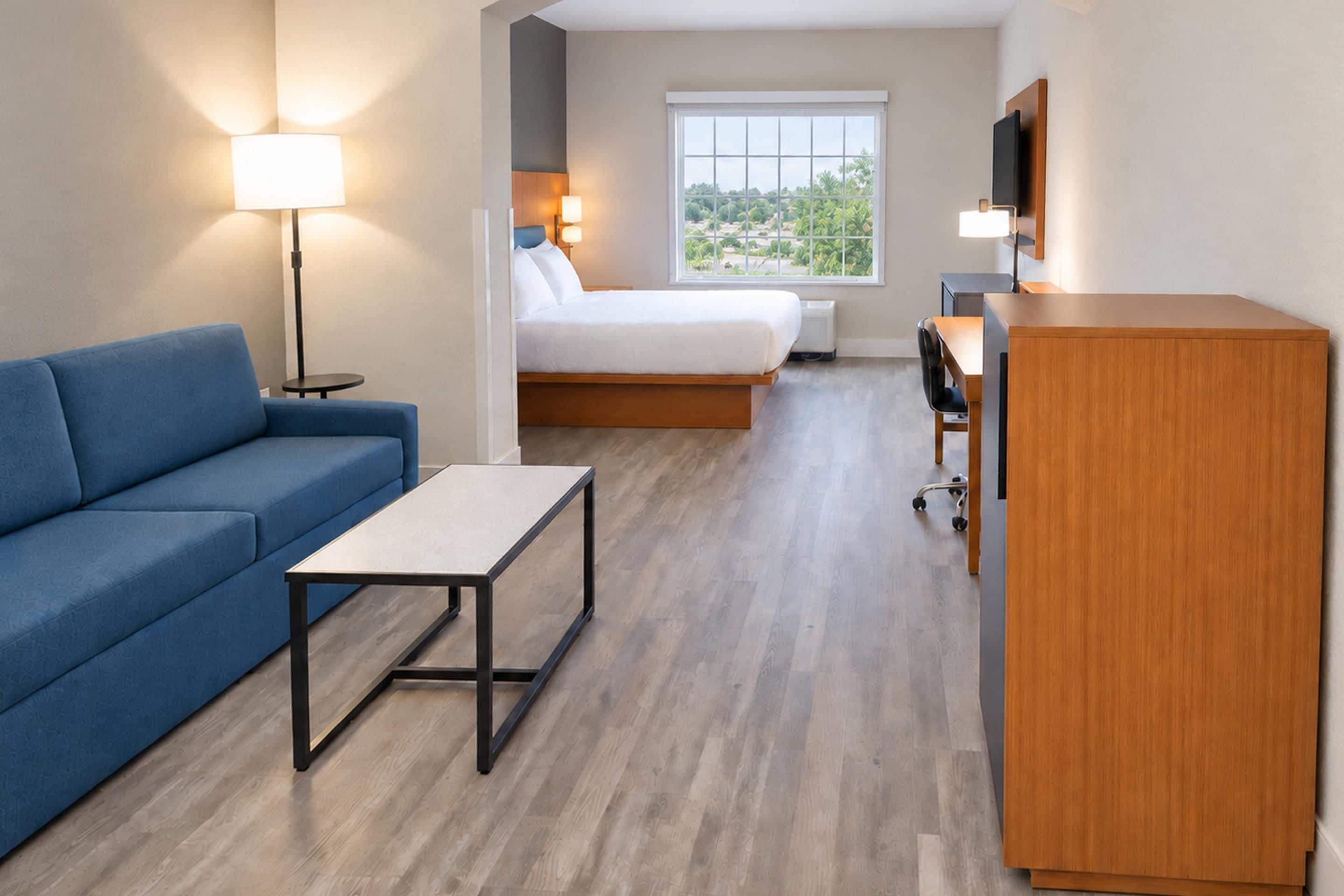 Habitación de hotel compacta con cama, sofá, escritorio y televisión.