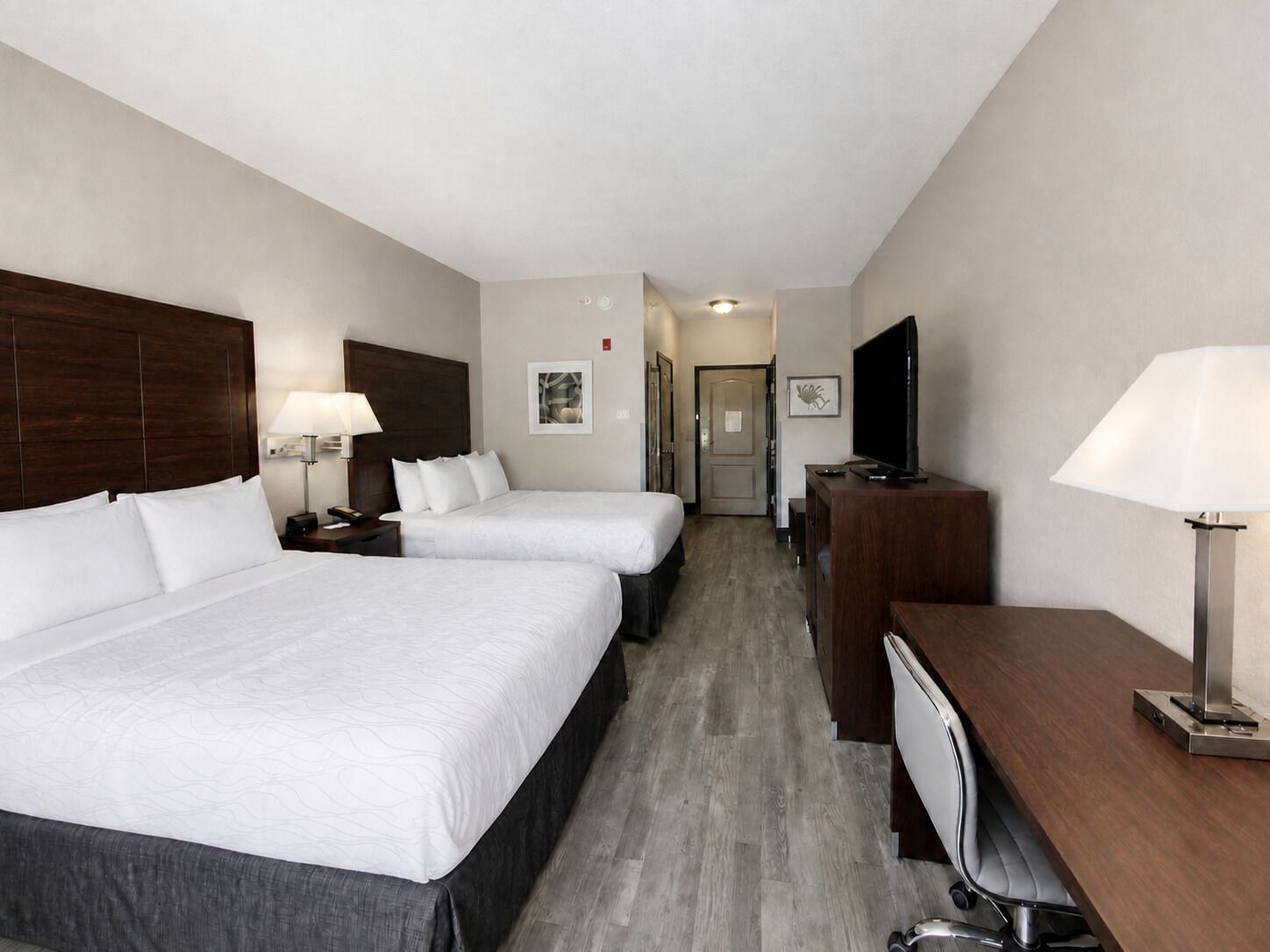 Een hotelkamer met twee bedden, een bureau, een televisie en een lamp.