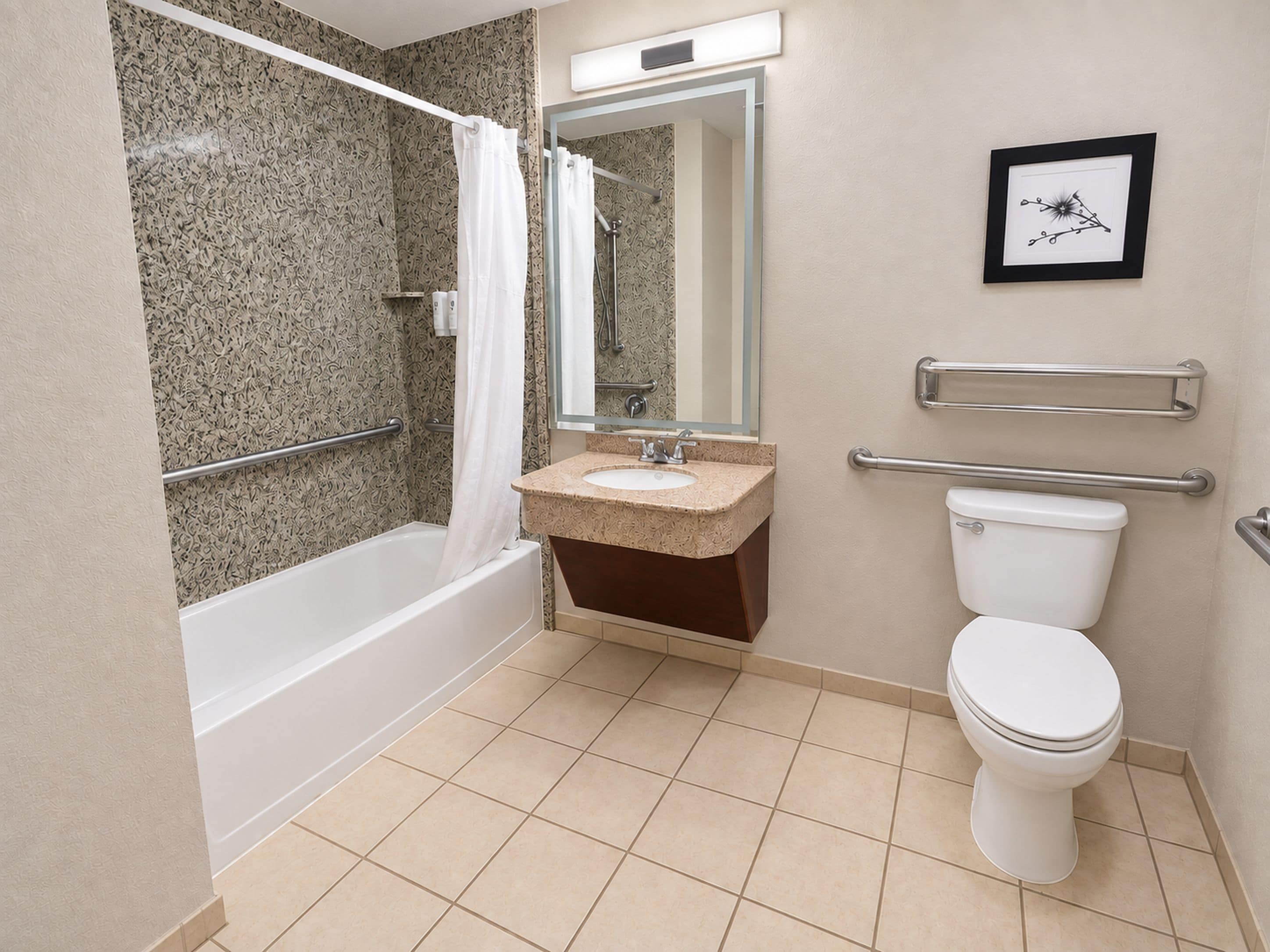A bathroom with a bathtub, sink, toilet, and handrails.