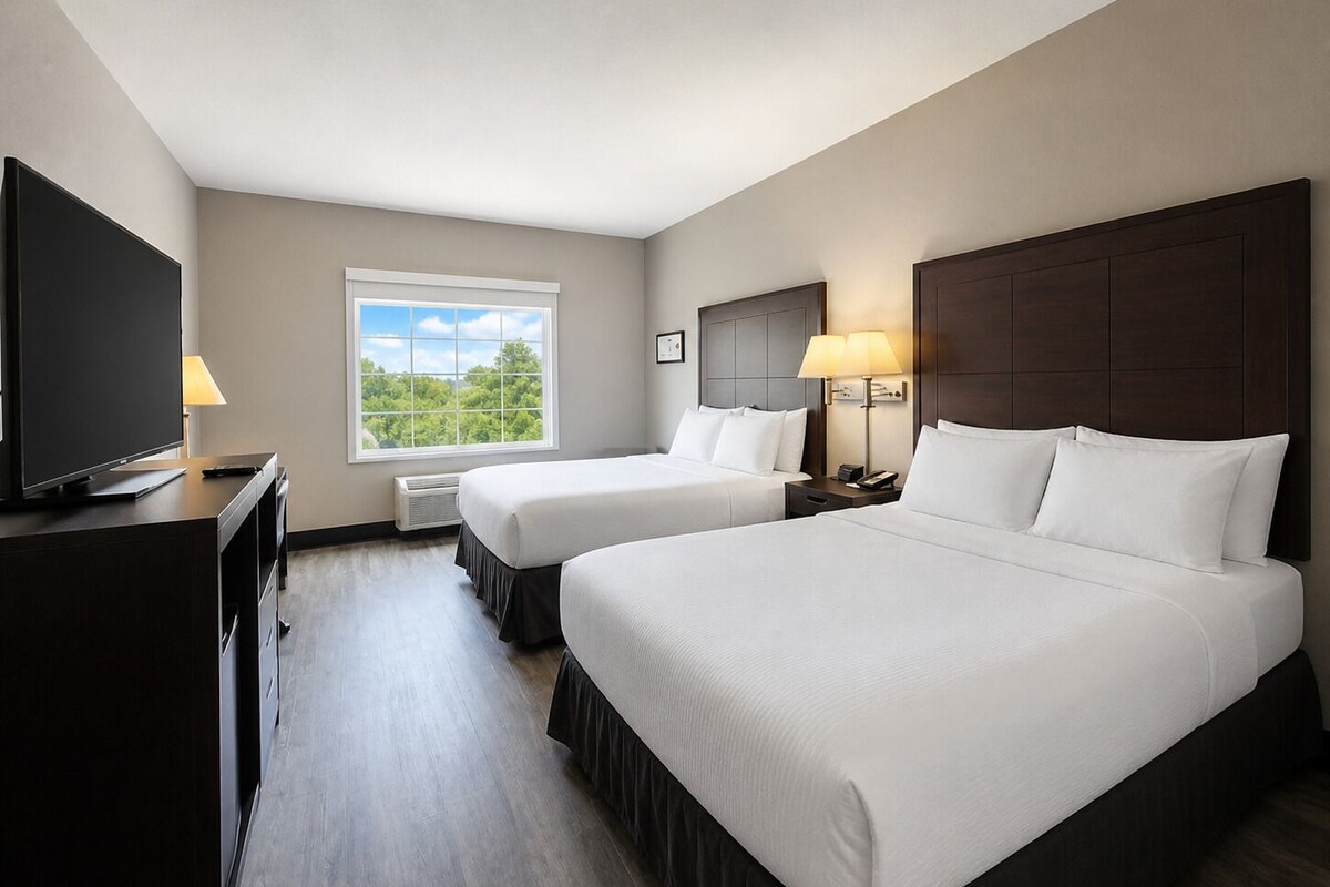 A hotel room with two beds, a television, a window with a view, and a desk with a lamp.