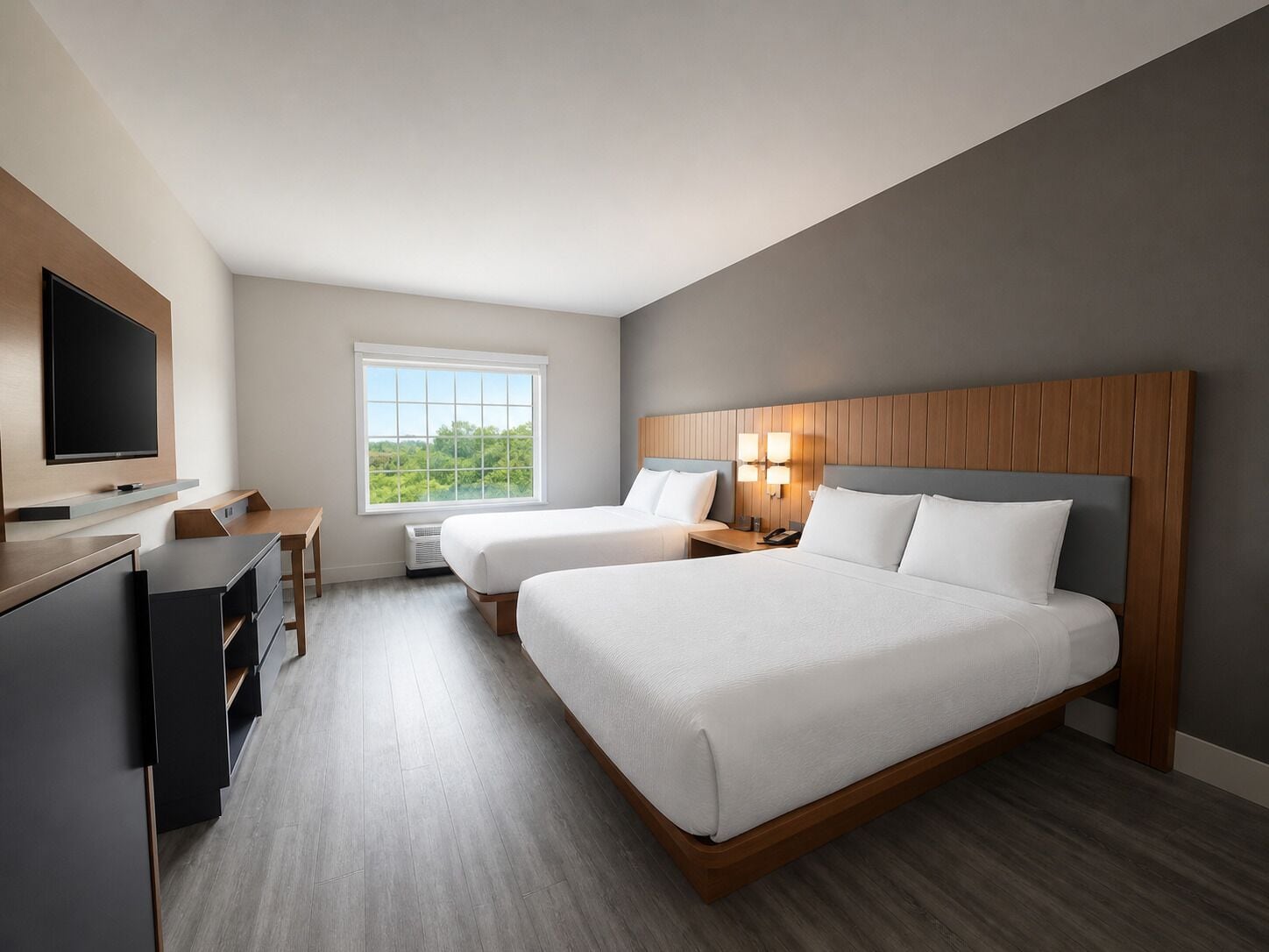 Habitación de hotel con dos camas, un escritorio, un televisor y ventana con vista.