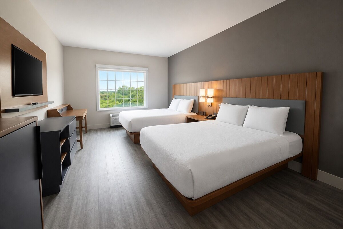 A hotel room with two beds, a desk, a television, and a window with a view.