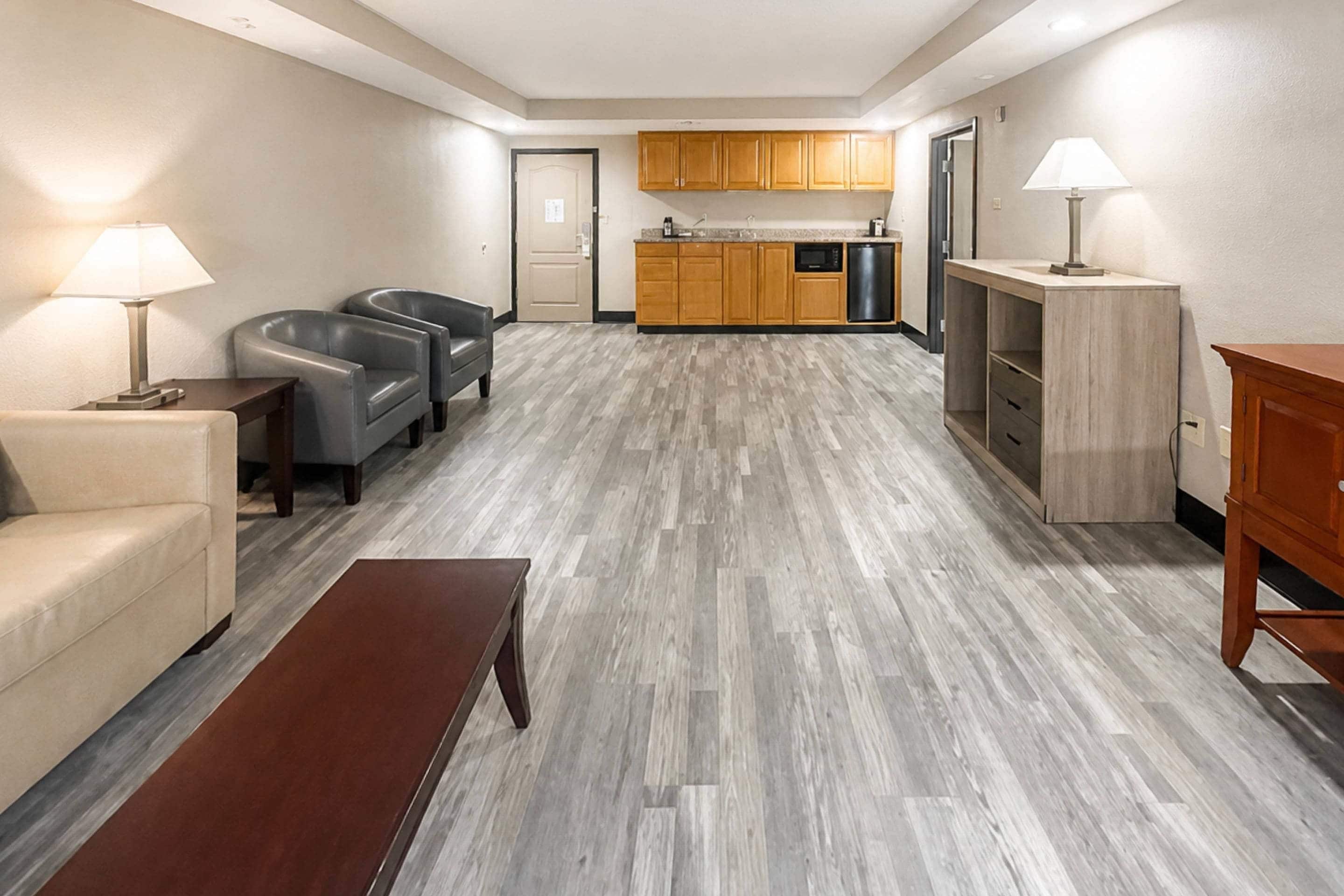 A hotel room with a seating area, a kitchenette, and a wooden floor.