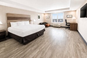 A hotel room with a large bed, a desk, a chair, a window, and a flat-screen TV.