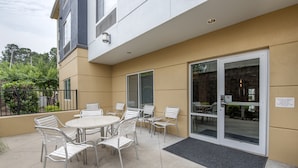 An outdoor patio with a round table and chairs, a glass door entrance, and a black mat at the door.