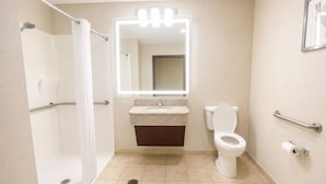 A bathroom with a shower, toilet, sink, and a mirror with lights.