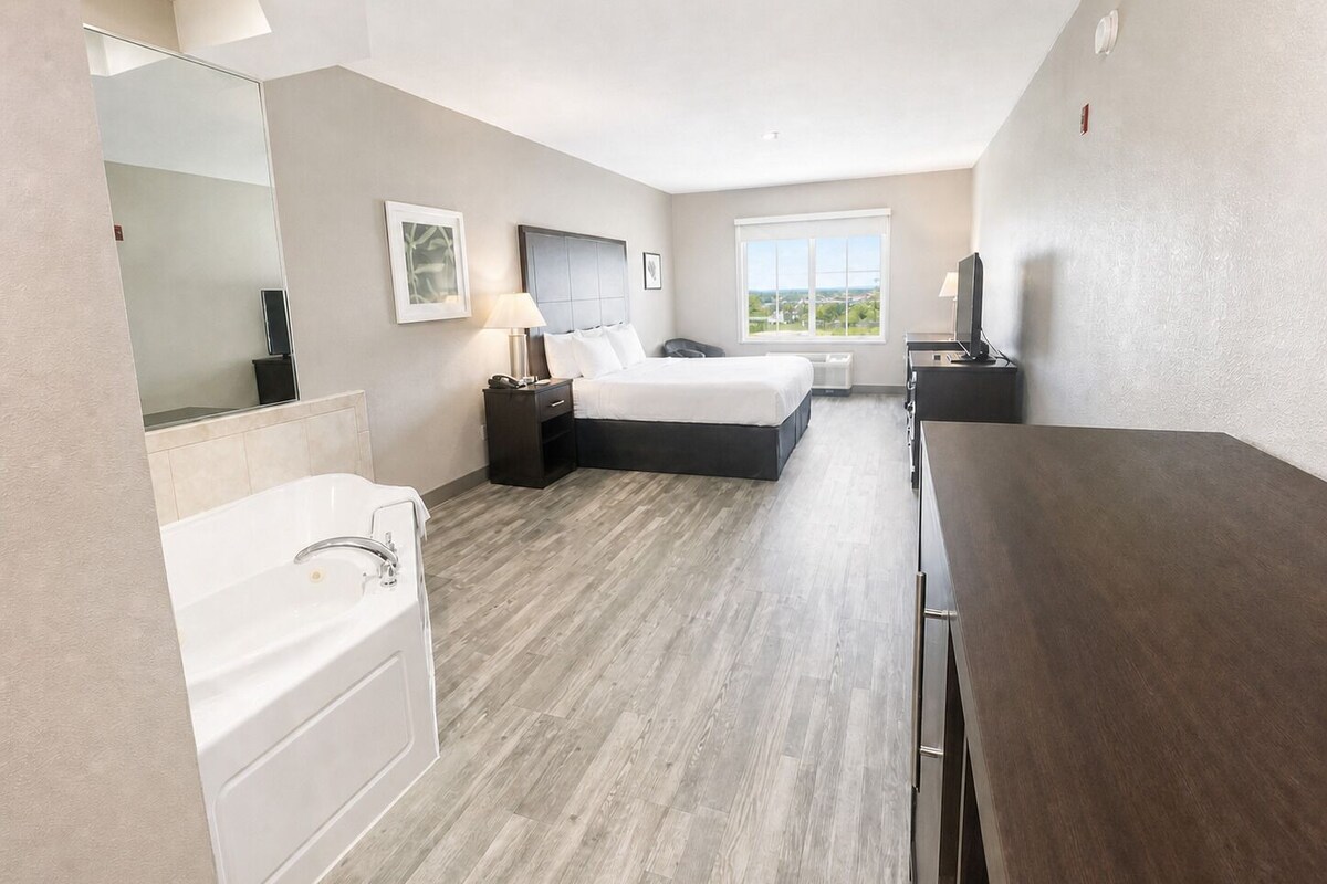 A hotel room with a bed, a desk, a chair, a bathroom with a bathtub, and a large window.