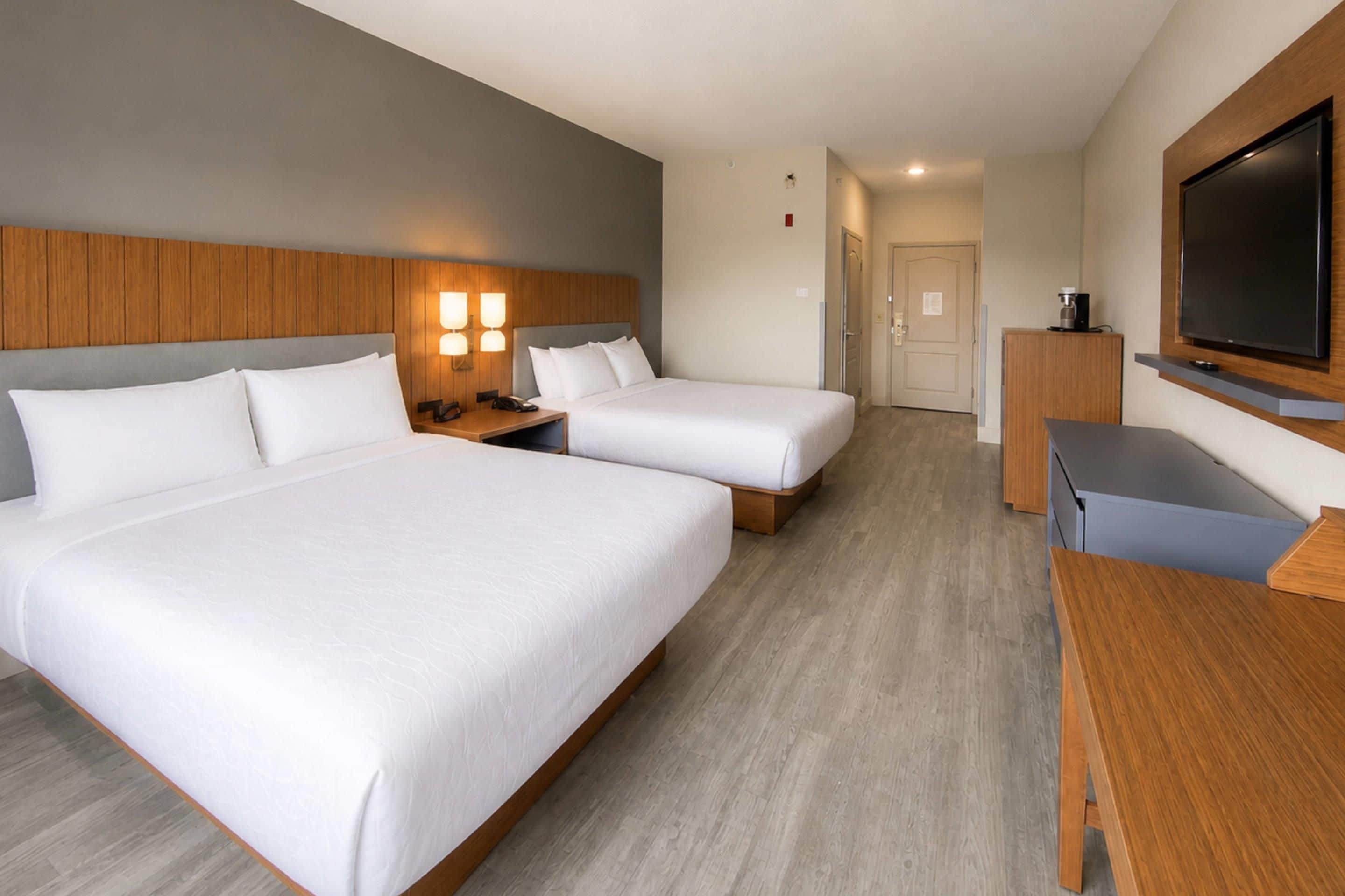 A hotel room with two beds, a desk, a television, and a coffee machine.