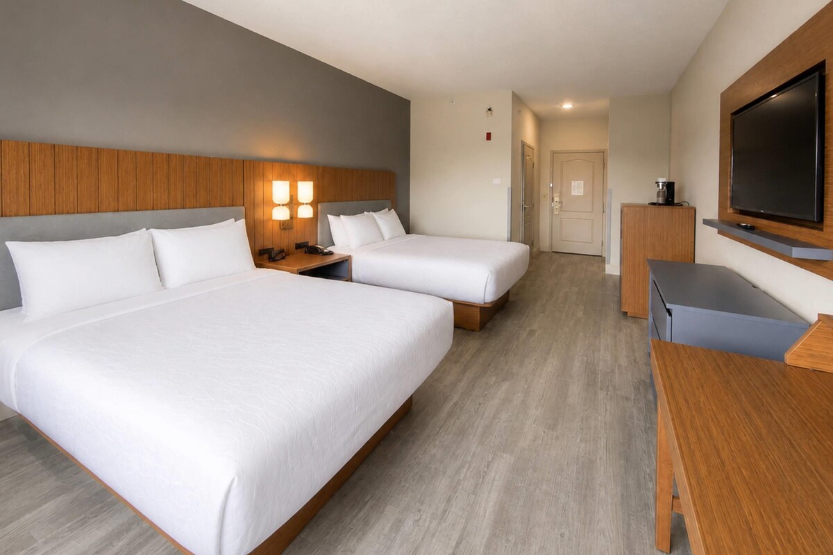 Een hotelkamer met twee bedden, een bureau, een televisie en een koffiezetapparaat.