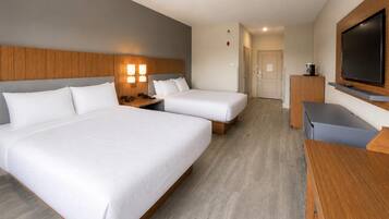 A hotel room with two beds, a desk, a television, and a coffee machine.