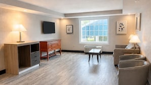 A modern living room with a wooden desk, a sofa, a small table, and a TV mounted on the wall.