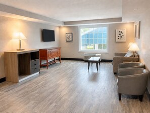 A modern living room with a wooden desk, a sofa, a small table, and a TV mounted on the wall. - Country Inn & Suites by Radisson, Pensacola West, FL (Pensacola)