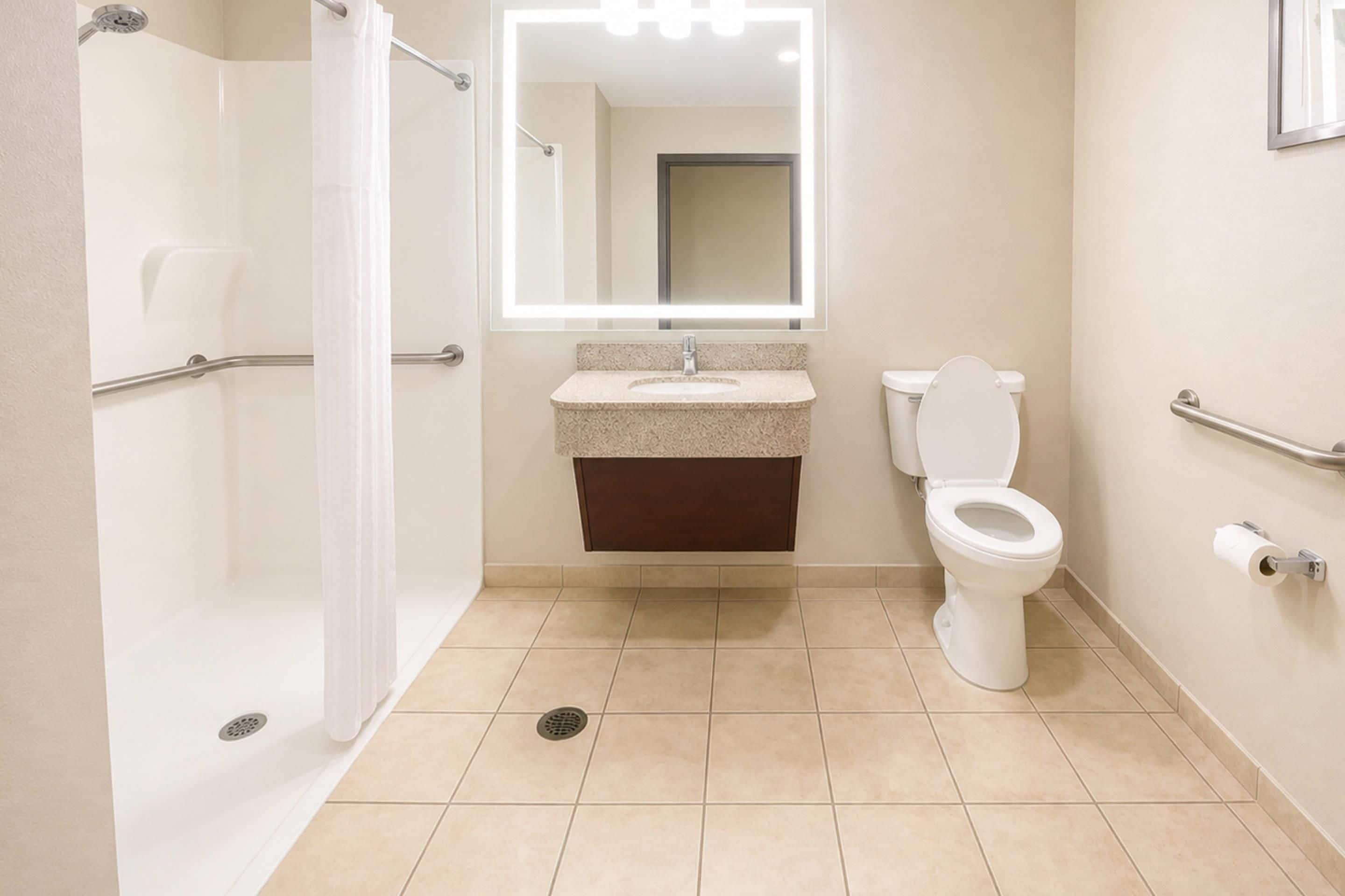 A bathroom with a shower, toilet, sink, and a mirror with lights.