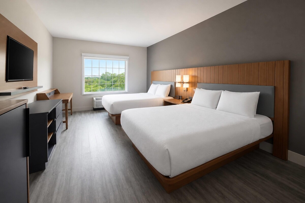 Een hotelkamer met een groot bed, een bureau, een televisie en een raam met uitzicht op groen.