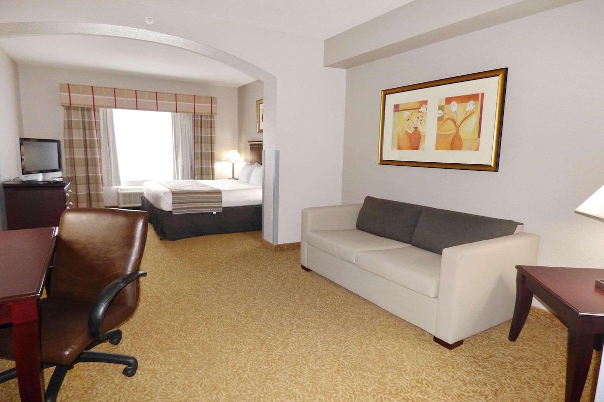 Hotelkamer met een bed, een witte bank, een bureau met stoel, een televisie en een lijst aan de muur.