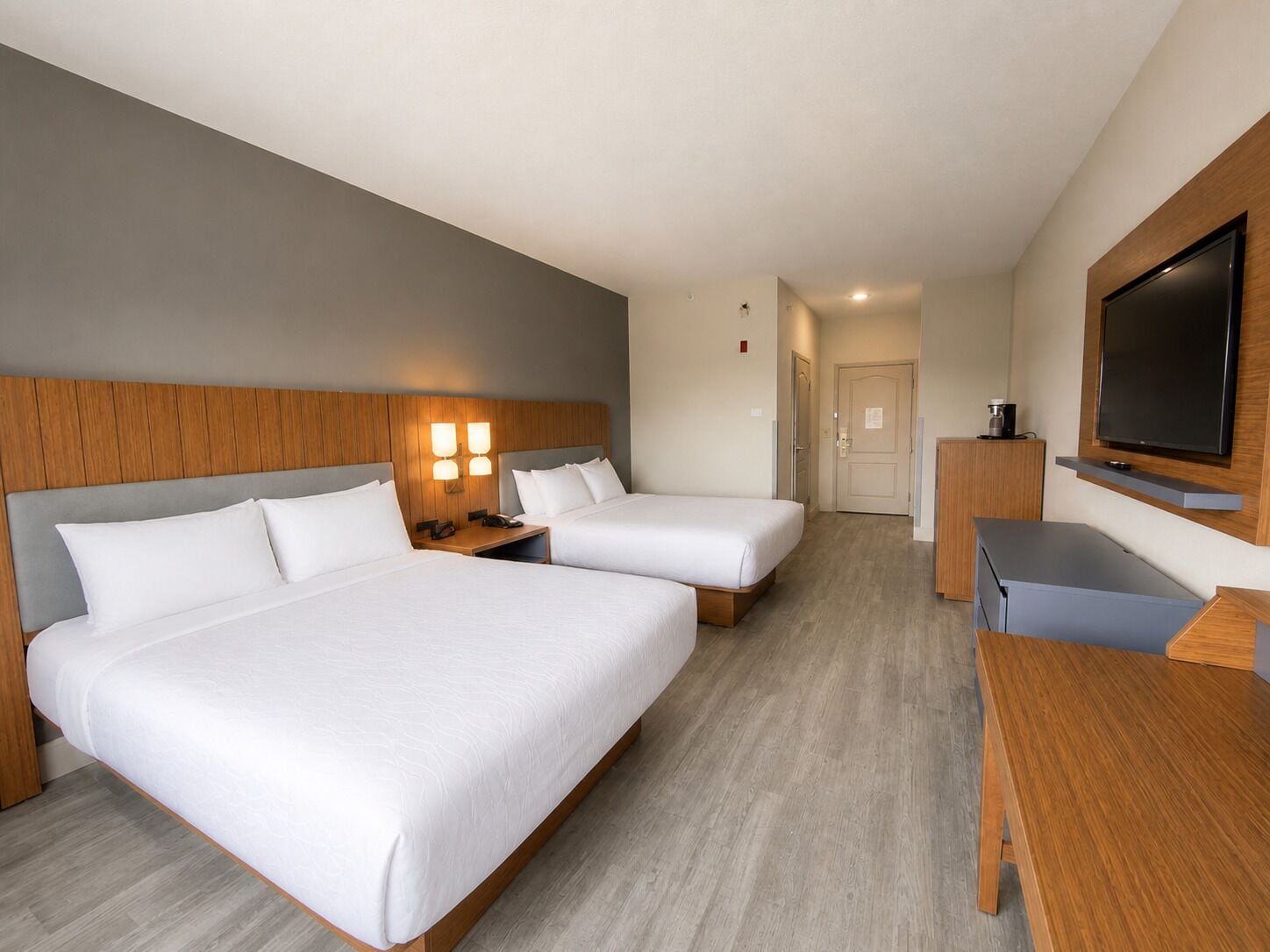 Habitación de hotel con dos camas, un escritorio, un televisor y una puerta que da a un baño.