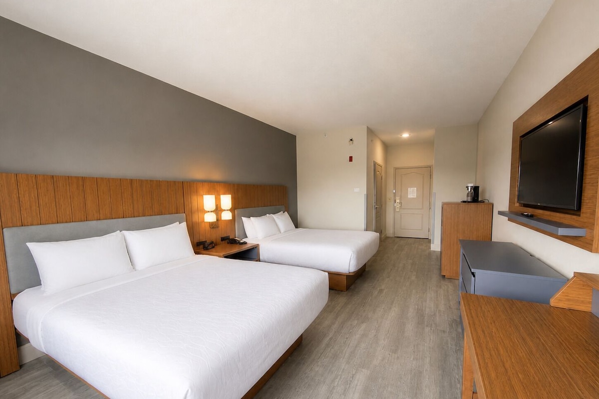 A hotel room with two beds, a desk, a TV, and a door leading to a bathroom.