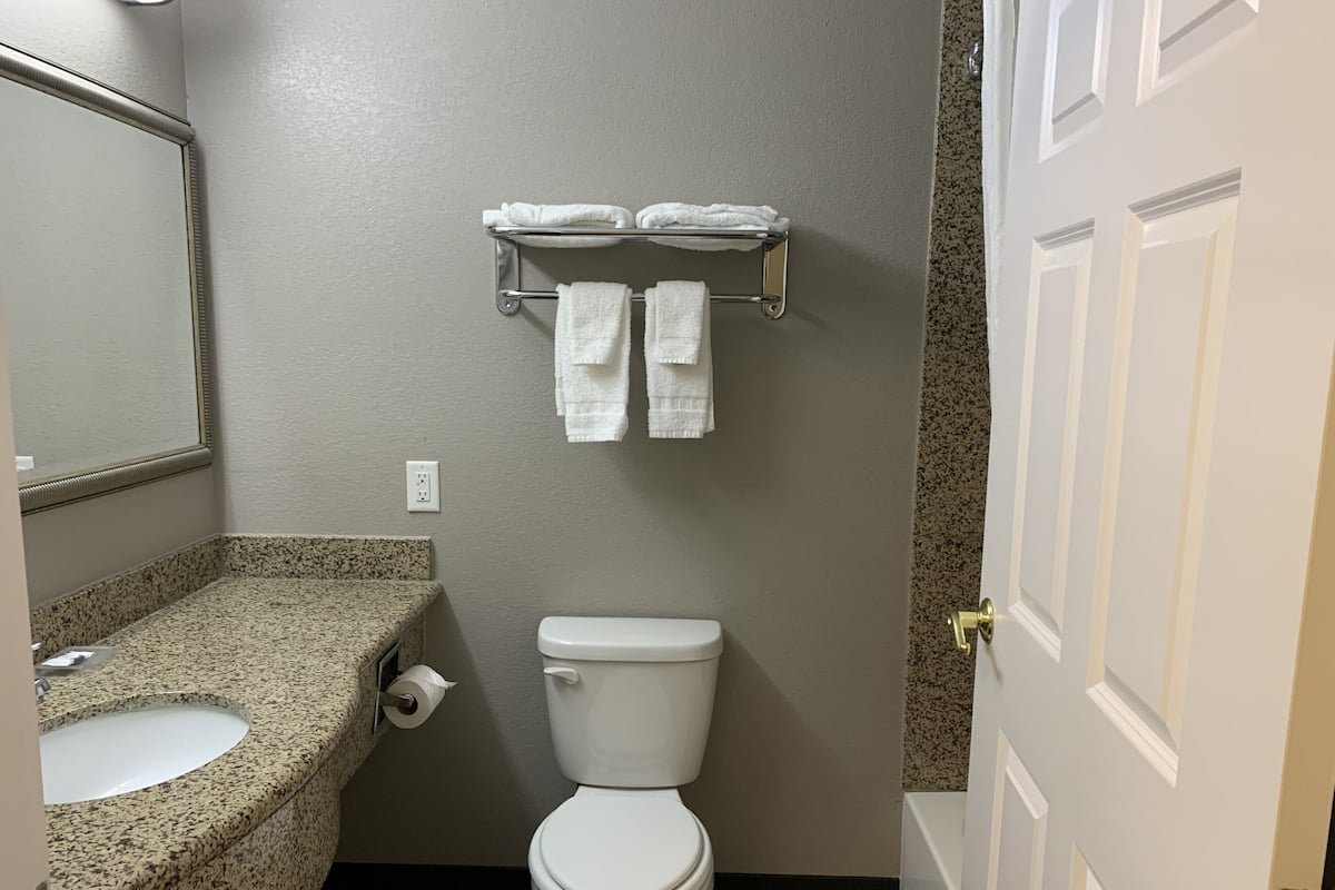 A bathroom with a granite countertop sink, a toilet, and a towel rack with two towels.