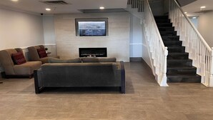 A modern living room with a sectional sofa, a flat-screen TV mounted on the wall, and a staircase with white railings.