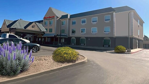 A hotel with a modern design, featuring a large parking lot and a landscaped area with shrubs.