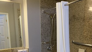 A bathroom with a granite countertop sink, a shower with a glass door, and a mirror with a light above it.