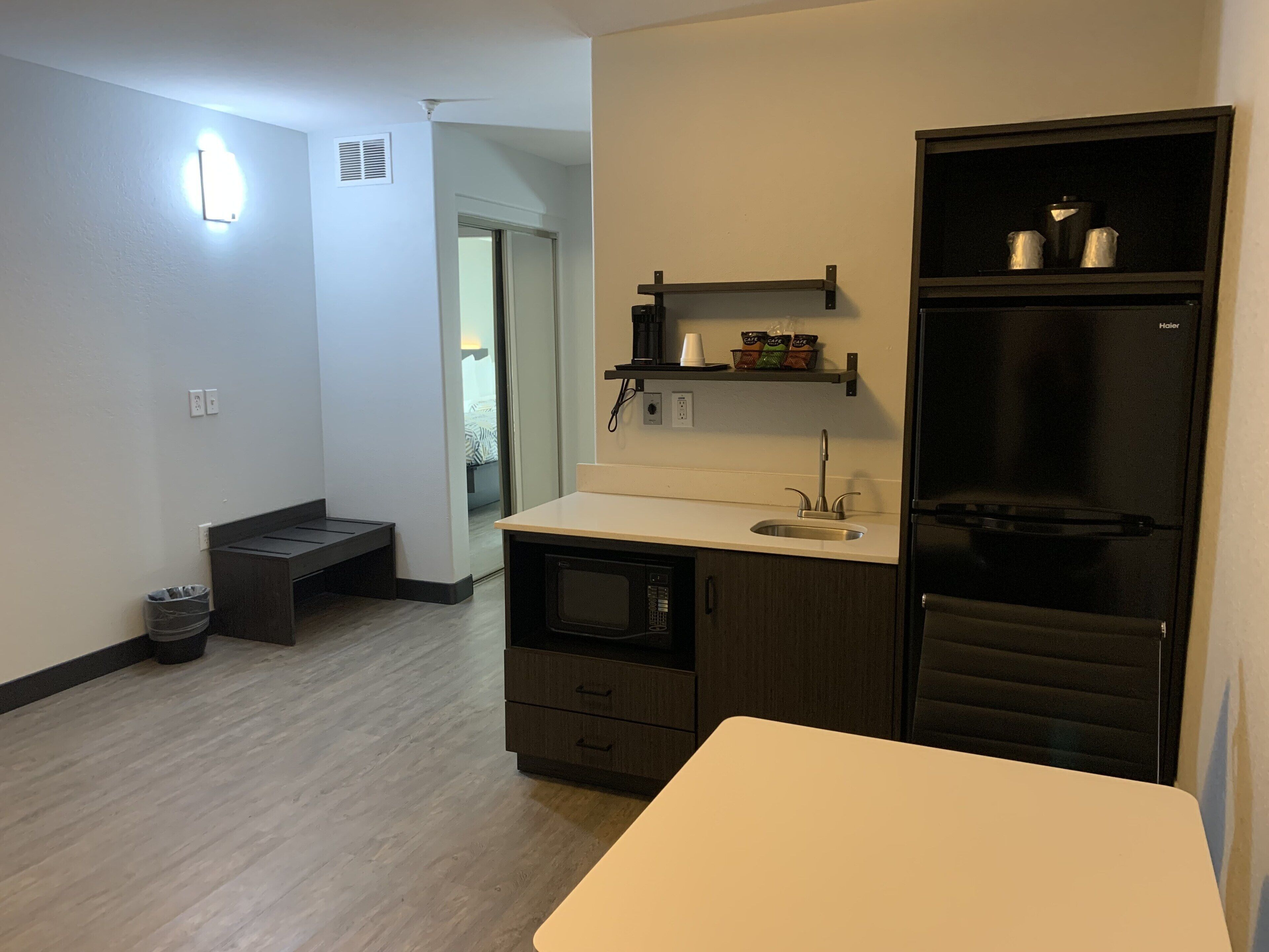 Una cocina compacta con refrigerador, un lavamanos y una pequeña encimera. Hay un basurero y un banco en la esquina.