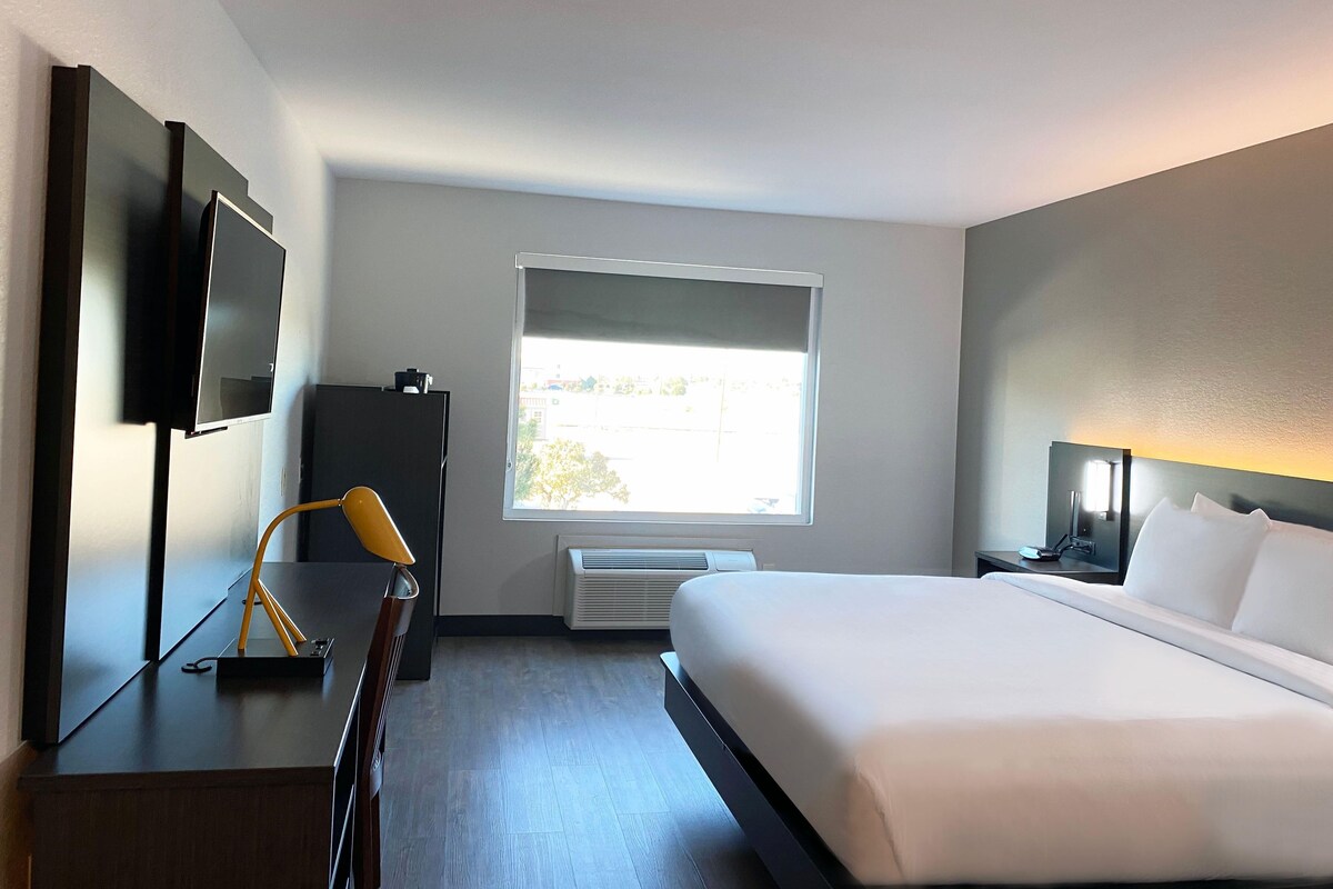 Een hotelkamer met een bed, een bureau, een stoel, een televisie, een raam en een lamp.