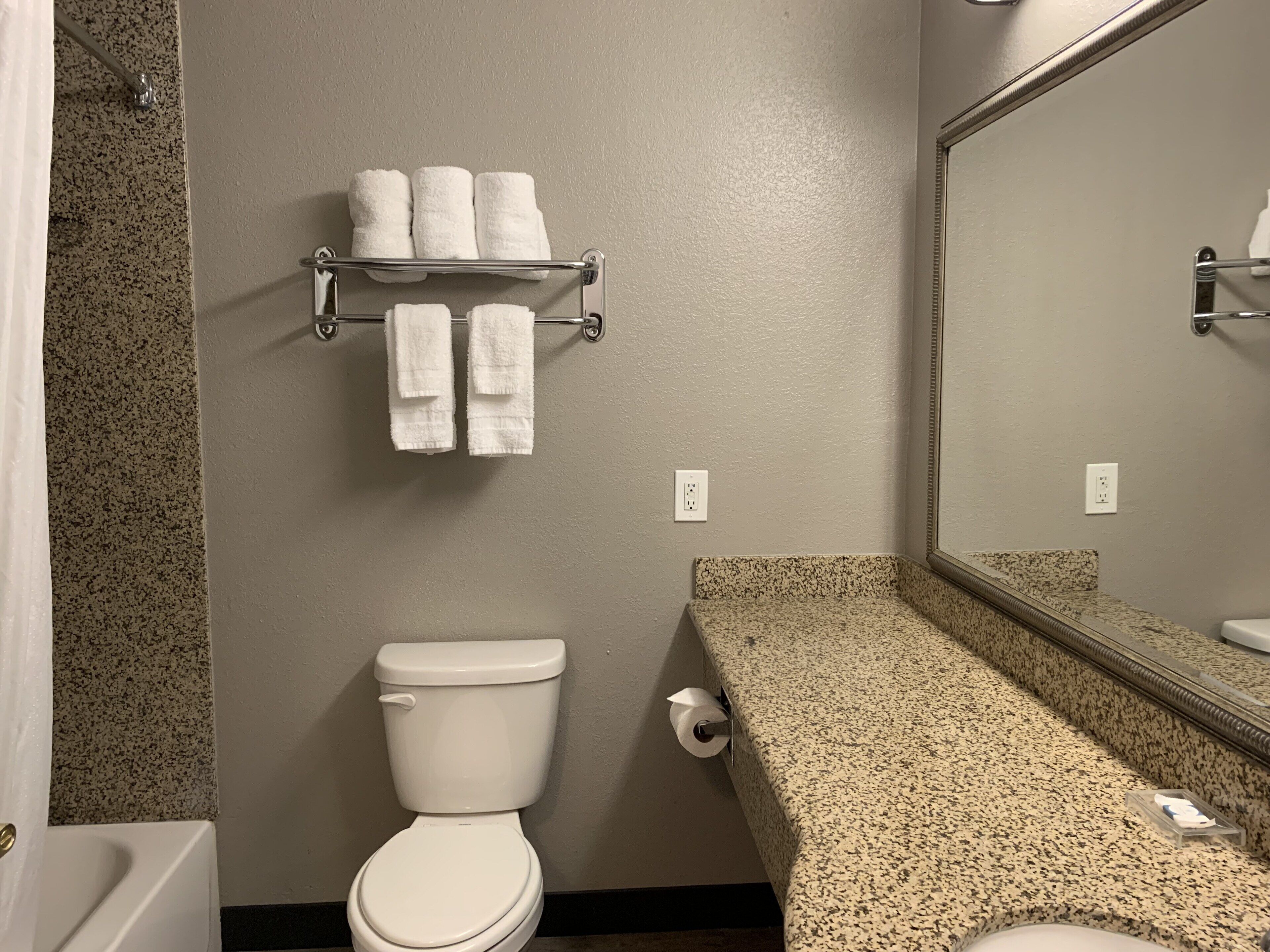 Un baño con inodoro, toallero con toallas, encimera y espejo.